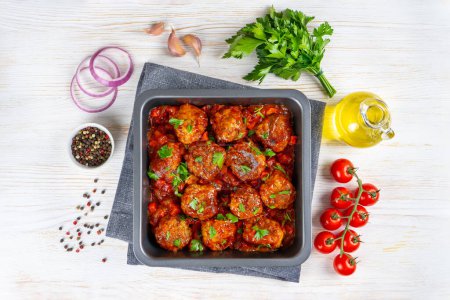 Téléchargez les photos : Homemade meatballs with tomato sauce and spices served in black pan on white wooden background. Tasty cooked meat balls made with minced beef and food ingredients. Top View, Flat lay. - en image libre de droit