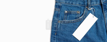 Foto de Front side pocket and price tag of blue jeans pants close-up isolated on white background, mockup, banner. Fashion, business, shopping, sale. Design detail, button and seams, clothing tag, copy space - Imagen libre de derechos