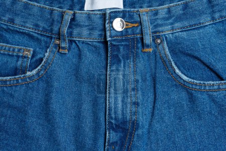 Foto de Front side and pockets of blue jeans pants close-up. Denim background, texture, wallpaper, fashion concept. Design detail, button and seams. - Imagen libre de derechos