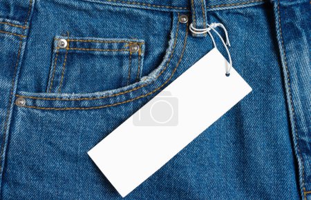 Foto de Front side pocket and price tag of blue jeans pants close-up. Denim background, texture, mockup. Fashion concept, business, shopping, sale. Design detail, button and seams, clothing tag, copy space - Imagen libre de derechos