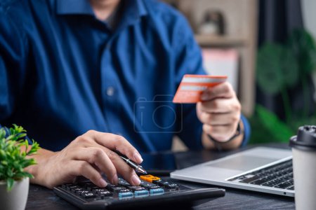 Persona que calcula los gastos con calculadora y tarjeta de crédito, indicativo de la gestión de las finanzas personales
