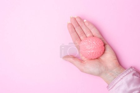 Hand hält rosa Gehirn isoliert auf rosa Hintergrund