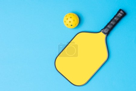 Gelber Pickleball-Schläger und Ball auf blauem Hintergrund. Horizontales Bildungs- und Sportplakat, Grußkarten, Kopfzeilen, Websit