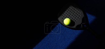 Foto de Raqueta y pelota de pádel profesional negra con iluminación natural sobre fondo azul. Cartel de tema deportivo horizontal, tarjetas de felicitación, encabezados, sitio web y aplicación - Imagen libre de derechos