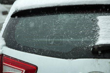 Foto de El cristal del coche despejado de una deriva de nieve se cubre de nuevo con una capa de nieve en una ventisca de invierno, un primer plano de la visión trasera del vehículo. - Imagen libre de derechos