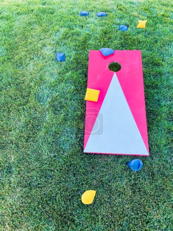 Red cornhole board lawn game leisure activity with bean bags on grass in summer