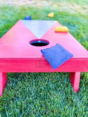 Red cornhole board lawn game leisure activity with bean bags on grass in summer