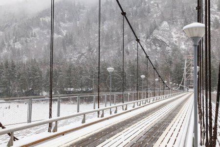 metalowy most wiszący dla samochodów i pieszych w górach Altai zimą ze śniegiem i mgłą na drzewach bez ludzi. Malownicze miejsce zimowy krajobraz