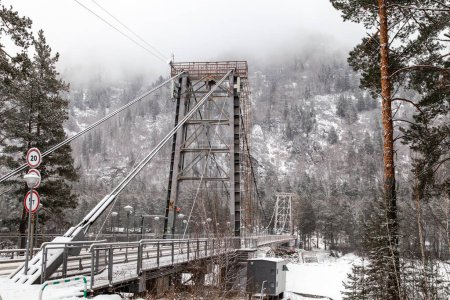 metalowy most wiszący dla samochodów i pieszych w górach Altai zimą ze śniegiem i mgłą na drzewach bez ludzi. Malownicze miejsce zimowy krajobraz