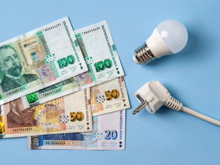 Téléchargez les photos : Fiche électrique, ampoule et sur fond bleu. Augmentation des coûts de l'électricité en Bulgarie. Crise de l'électricité, factures d'énergie coûteuses, hausse du concept de prix de l'électricité. Vue du dessus. - en image libre de droit