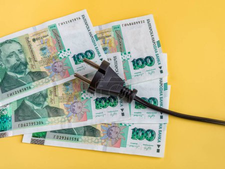 Black electric plug on one hundred bulgarian lev banknotes. Rise in energy prices in Bulgaria. Increasing of electricity costs, power crisis, inflation concepts. Payment of electricity bills. Top view.