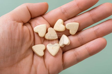 Pet vitamin pills on a woman hand palm. Heart shaped nutritional supplements for cats and dogs macro. Veterinary vegan treats for domestic animals. Medicine and vitamins for pets concept. Top view.