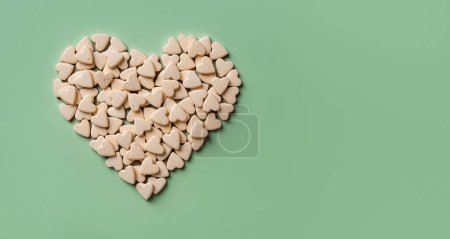 Heart shaped pet nutritional supplements over green background. Vitamin vegan treats for cats and dogs macro. Veterinary natural pills concept. Medicine for domestic animals. Copy space. Top view.