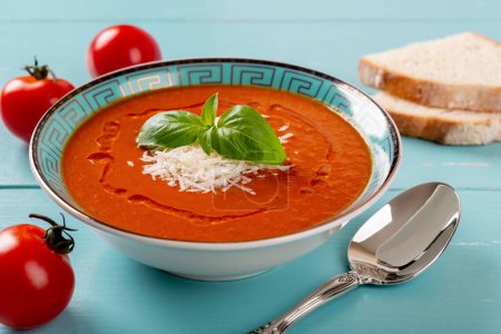 Photo for Hot tomato soup and spoon over turquoise wooden table. Homemade soup of pureed tomatoes with grated parmesan and fresh basil. Healthy vegetarian dish. Mediterranean cuisine. Closeup. - Royalty Free Image