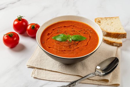 Photo for Bowl of hot tomato soup over marble background. Hot vegetable soup puree, spoon and bread. Healthy vegetarian dish of roasted tomatoes with garlic and basil. Mediterranean cuisine. Top view. - Royalty Free Image