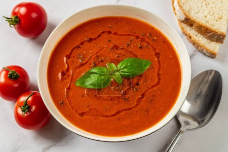 Photo for Hot tomato soup in a white bowl closeup. Freshly made vegetable dish of pureed tomatoes, garlic and basil ready to eat. Healthy vegetarian dish. Mediterranean cuisine. Top view. - Royalty Free Image