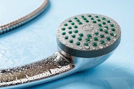 Pomme de douche main humide macro. L'eau tombe sur une pomme de douche portable en métal et un tuyau flexible sur fond bleu. Prendre une douche, le lavage, l'hygiène et le concept de bain. Gros plan.