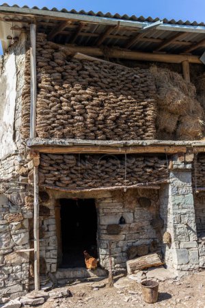 Téléchargez les photos : Un bâtiment en pierre avec un tas de fumier brun et des piles de foin. Une ancienne grange traditionnelle au Daghestan, en Russie - en image libre de droit
