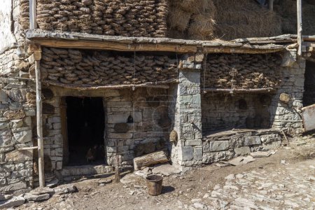 Téléchargez les photos : Un bâtiment en pierre avec un tas de fumier brun et des piles de foin. Une ancienne grange traditionnelle au Daghestan, en Russie - en image libre de droit