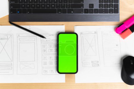 Téléchargez les photos : Sketch of wireframe for website. Women designer working on a mobile application, holding in hand phone with green screen - en image libre de droit
