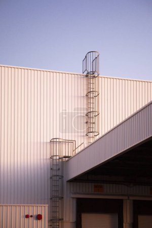 Photo for Stationary steel ladder offers vertical access a white warehouse wall, providing a climbing solution. - Royalty Free Image