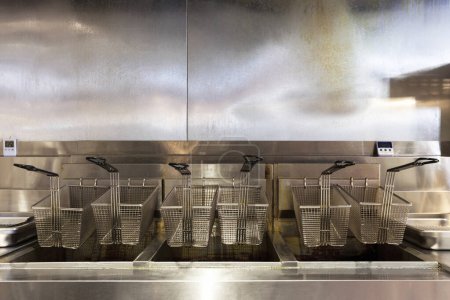 Téléchargez les photos : Les paniers de friteuse au ralenti reposent sur une surface en acier inoxydable, marquée de taches de graisse persistantes. - en image libre de droit