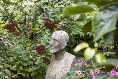 Téléchargez les photos : Statue en pierre entourée de belles fleurs dans un jardin serein - en image libre de droit