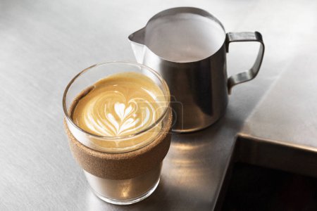Téléchargez les photos : Café Latte à côté d'un pichet à lait en acier inoxydable sur un comptoir en métal. - en image libre de droit