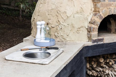 Clay pizza oven is set in an outdoor home setting with kitchen utensils nearby, ready for cooking.