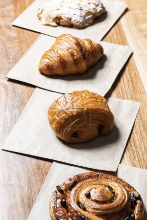 Téléchargez les photos : Variété de pâtisseries de boulangerie, y compris des croissants, des rouleaux de chocolat et des raisins secs en spirale danois, disposés sur une toile de fond en bois. - en image libre de droit