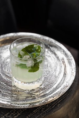 Téléchargez les photos : Cocktail mojito garni de feuilles de menthe fraîche et de glaçons sur un plateau argenté. - en image libre de droit