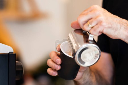 Téléchargez les photos : Barista verser du lait cuit à la vapeur dans une tasse de café noir à emporter. - en image libre de droit