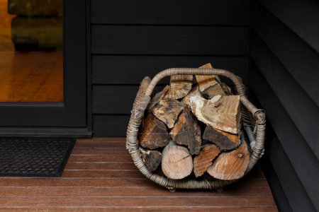 Téléchargez les photos : Empilement de bois de chauffage dans un panier en osier placé près de l'entrée d'une maison. - en image libre de droit