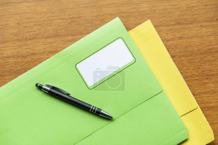 Téléchargez les photos : Dossiers de manila colorés avec un stylo noir placé au-dessus d'eux, disposés sur une table en bois. - en image libre de droit