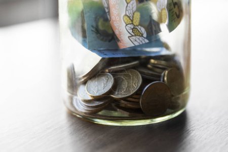 Tarro de vidrio lleno de monedas y dinero, utilizado para ahorrar.