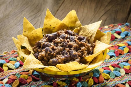 Téléchargez les photos : Délicieux chili con carne mexicain avec des nachos sur une nappe colorée au crochet, sur un fond de table en bois - en image libre de droit