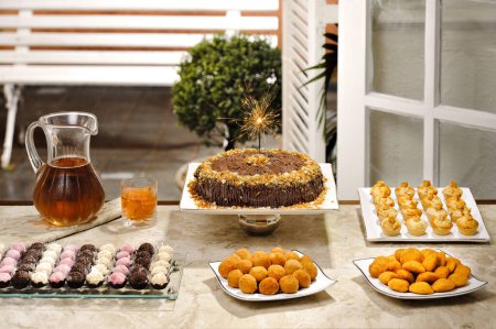 Photo for Birthday table setting with cake, a sparkler, candies, soda and brazilian snacks - Royalty Free Image