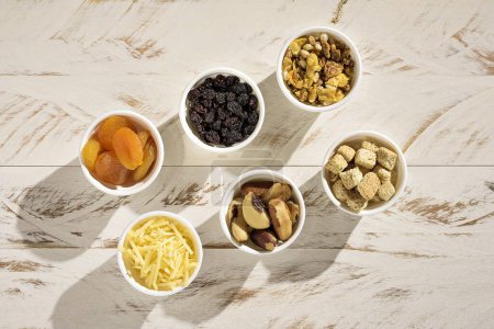 Téléchargez les photos : Six ramequins aux céréales, croûtons, noix du Brésil, parmesan, abricot turc et raisins secs, sur une table en bois rustique blanc - en image libre de droit