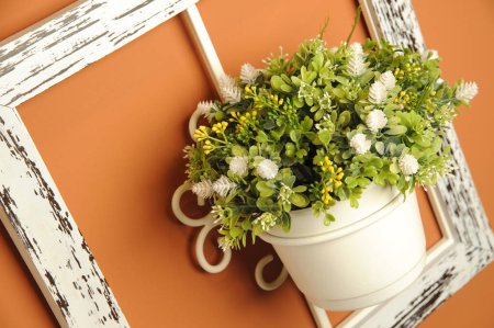 White vase with decorative plastic flowers, on a rustic wooden frame, on a orange wall