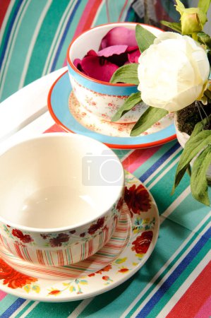 Two colorful ceramic cups with flower pattern with rose petals inside, on stripes background