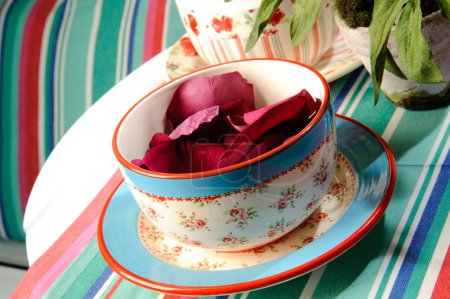 Colorful ceramic cup with flower pattern with rose petals inside, on stripes background