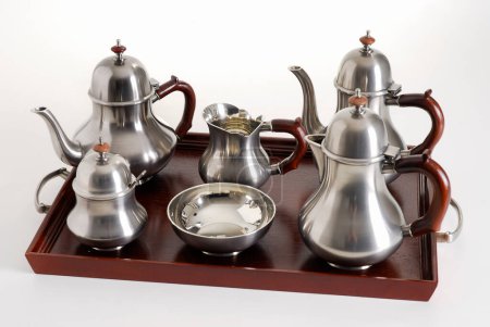 Silver tea and coffe pots set on a dark wood tray, isolated