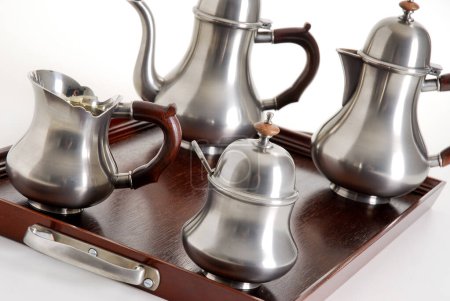 Close up of silver tea and coffe pots set on a dark wood tray, isolated