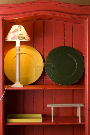 Étagère en bois peinte en rouge avec une paire de sous-plat vert et jaune, et une lampe