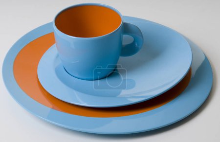 Foto de Taza azul y naranja moderna, con platos coloridos debajo - Imagen libre de derechos