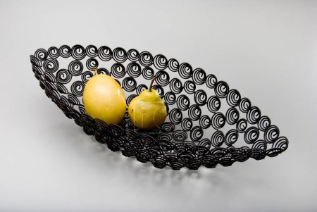 Foto de Pera y una fruta de la pasión dentro de un recipiente de fruta de metal negro en forma de canoa, con espirales recortadas, aisladas en blanco - Imagen libre de derechos