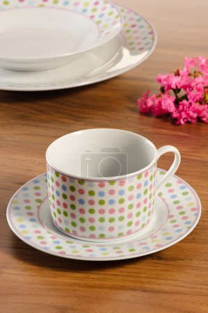 Foto de Taza de café con platillo en una mesa de madera con juego de platos en el fondo - Imagen libre de derechos
