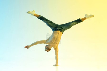 Foto de Hombre fuerte de cuerpo completo con las piernas abiertas torso desnudo y haciendo truco handstand durante el rendimiento contra la iluminación de neón colorido - Imagen libre de derechos