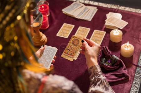 Photo for High angle of crop anonymous female fortune teller picking sun tarot card while sitting at table with burning candles and crystal - Royalty Free Image