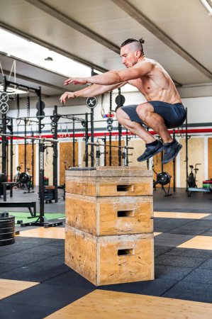 Photo for Full body side view of shirtless muscular male athlete doing box jump exercise during intense workout in gym - Royalty Free Image